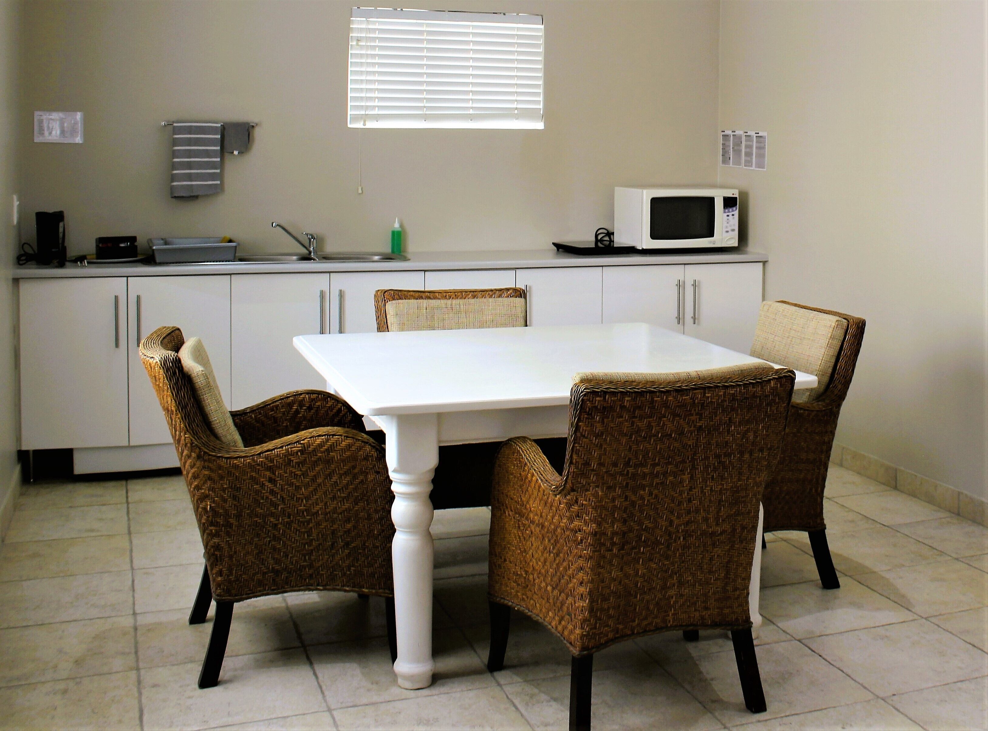 A small kitchen with white cabinets, a white table, and wicker chairs.