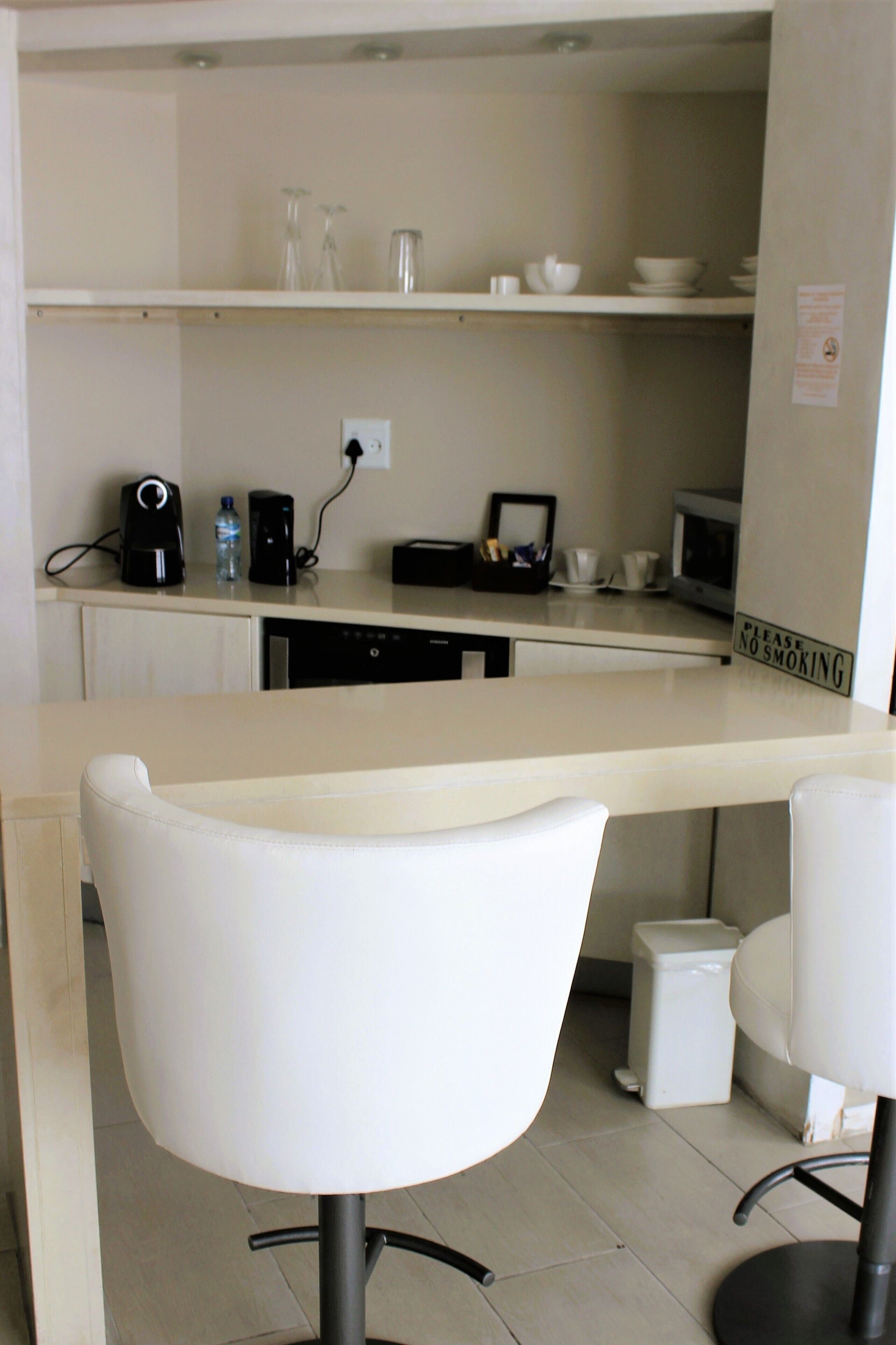 A modern kitchen with a white countertop, a coffee maker, a microwave, and a "Please No Smoking" sign.