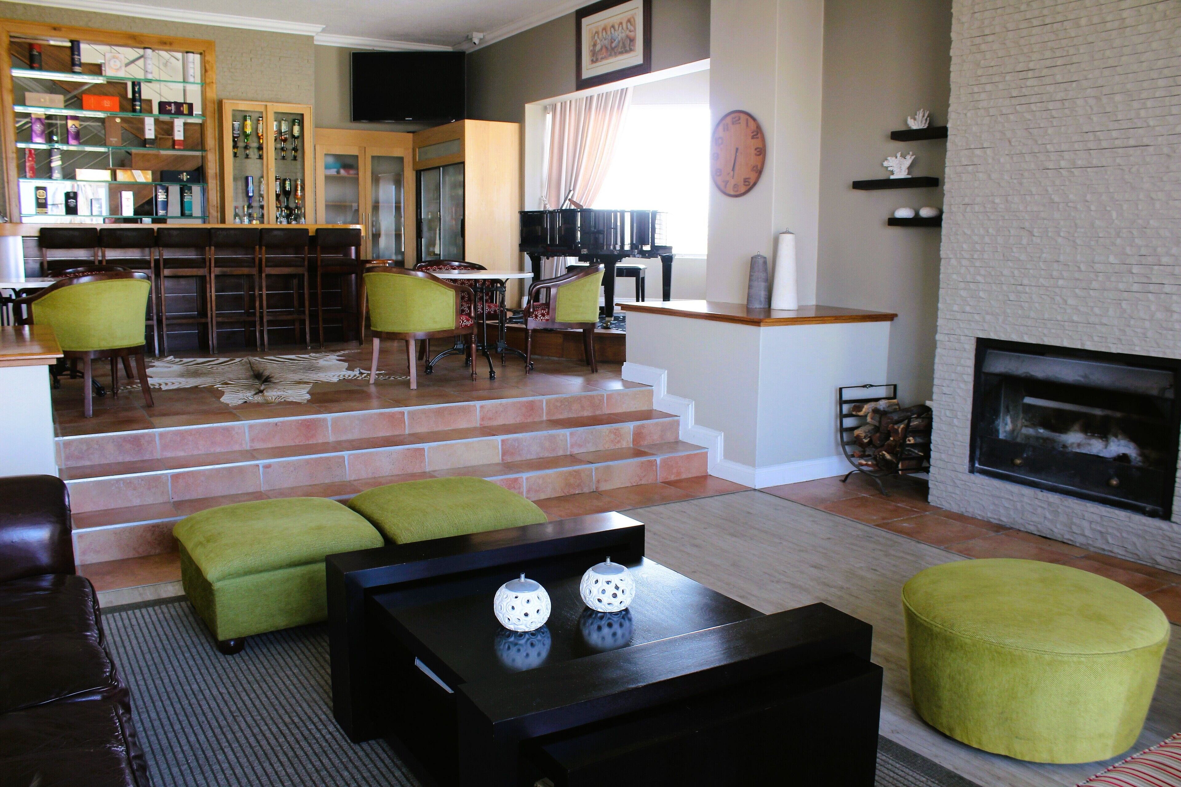 A spacious living room with a piano, green ottomans, a fireplace, and a bar area with shelves.
