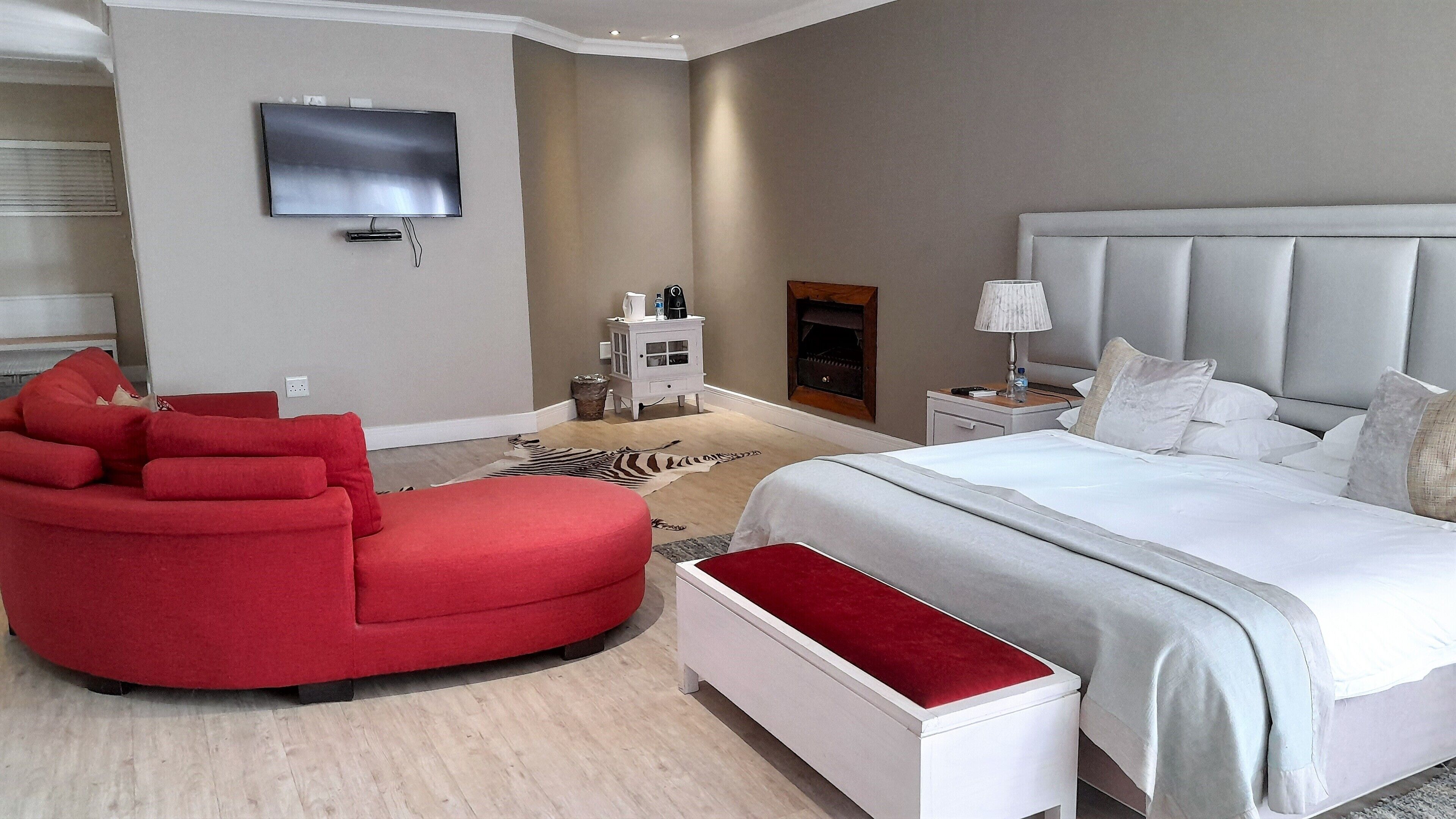 A modern hotel room with a large bed, a red armchair, a small white nightstand, a television mounted on the wall, and a zebra-patterned rug.