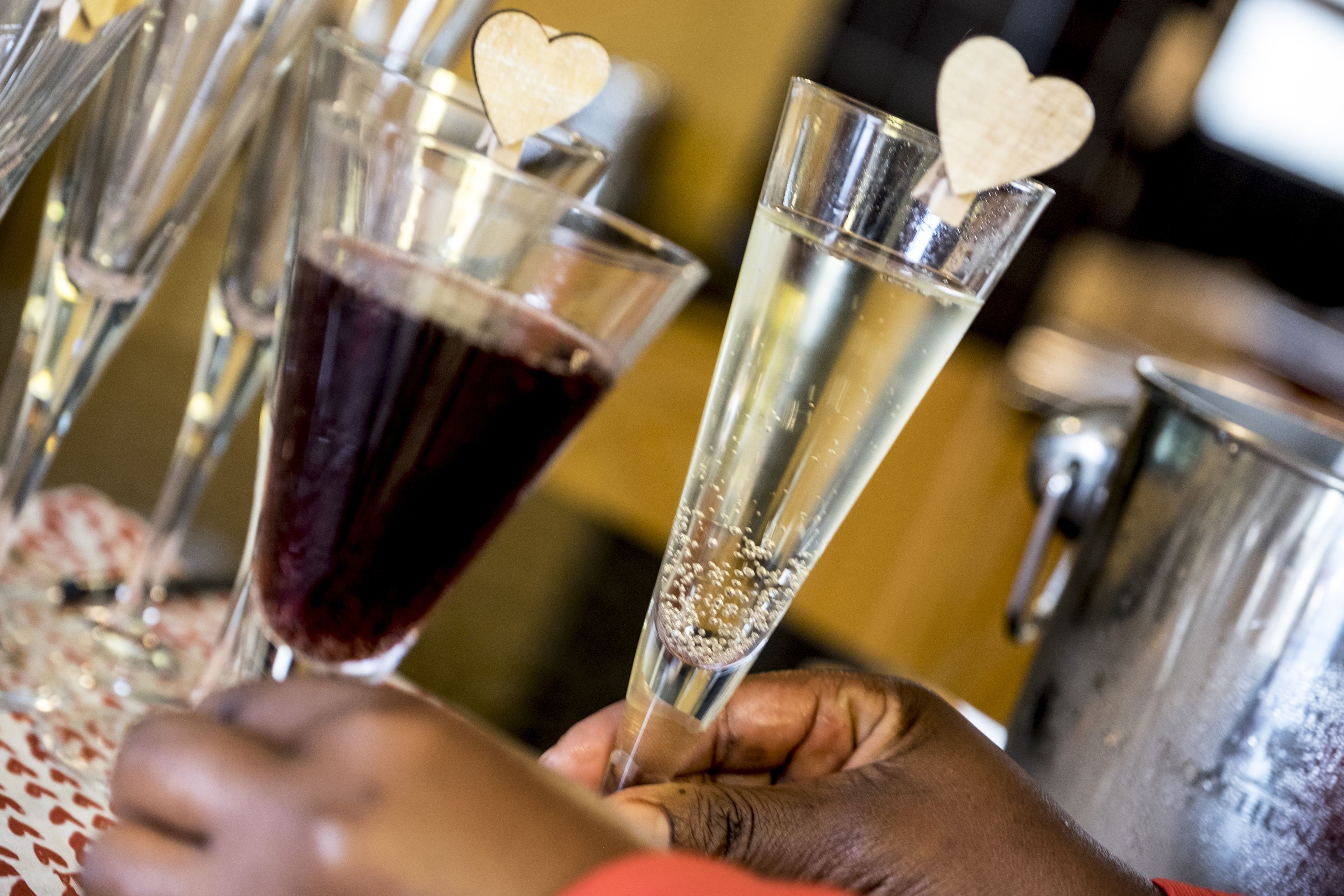 A close-up of hands holding champagne flutes with heart-shaped ice cubes, a metallic pitcher, and a table with a patterned tablecloth.