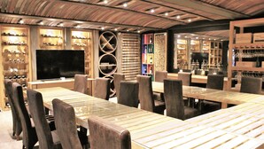 A restaurant with wooden tables and chairs, a large TV screen, and shelves with bottles. - Atlantic Villa Boutique Guesthouse (Swakopmund)