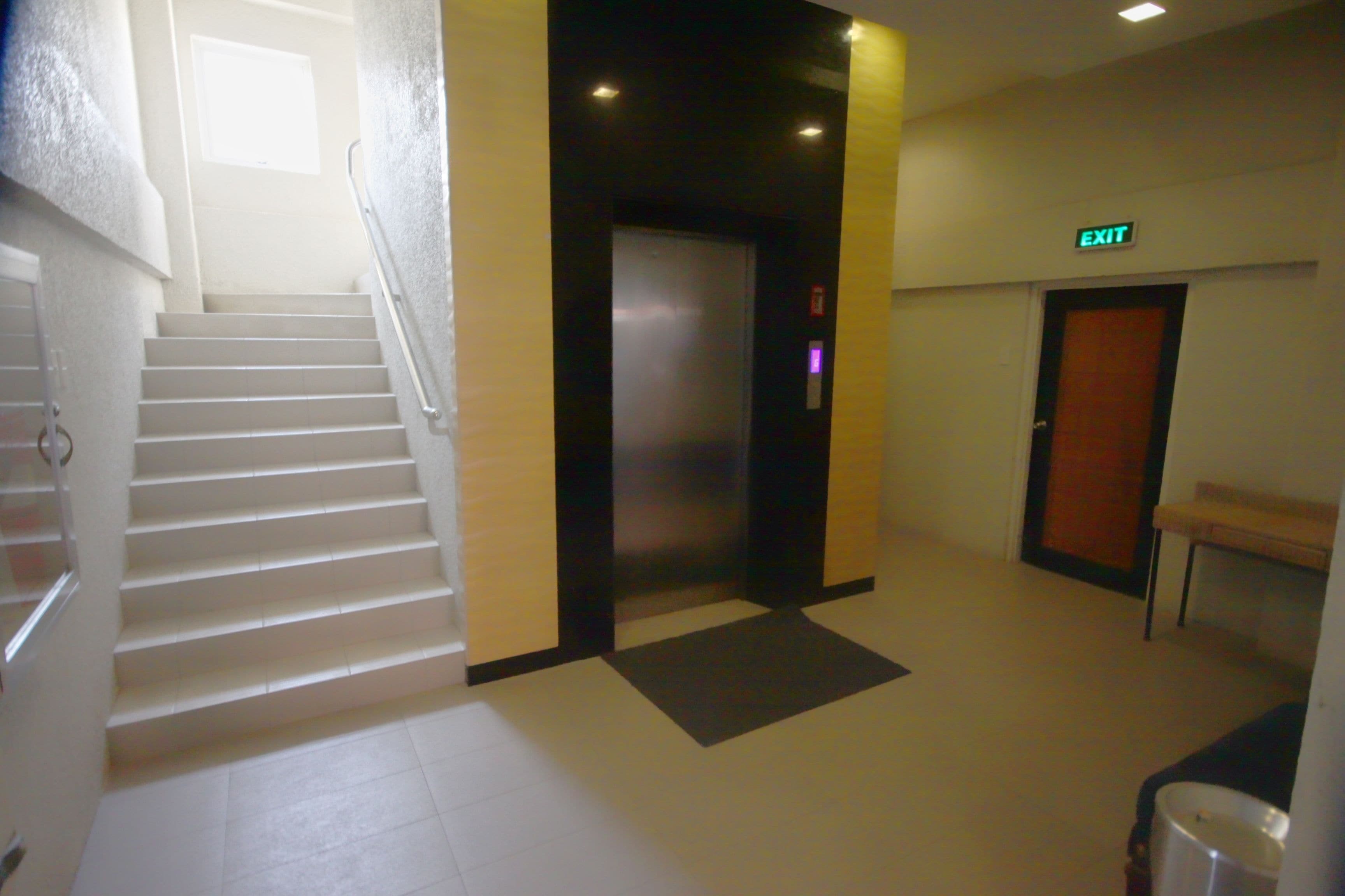 A hotel lobby with a staircase, an elevator, and an exit sign.