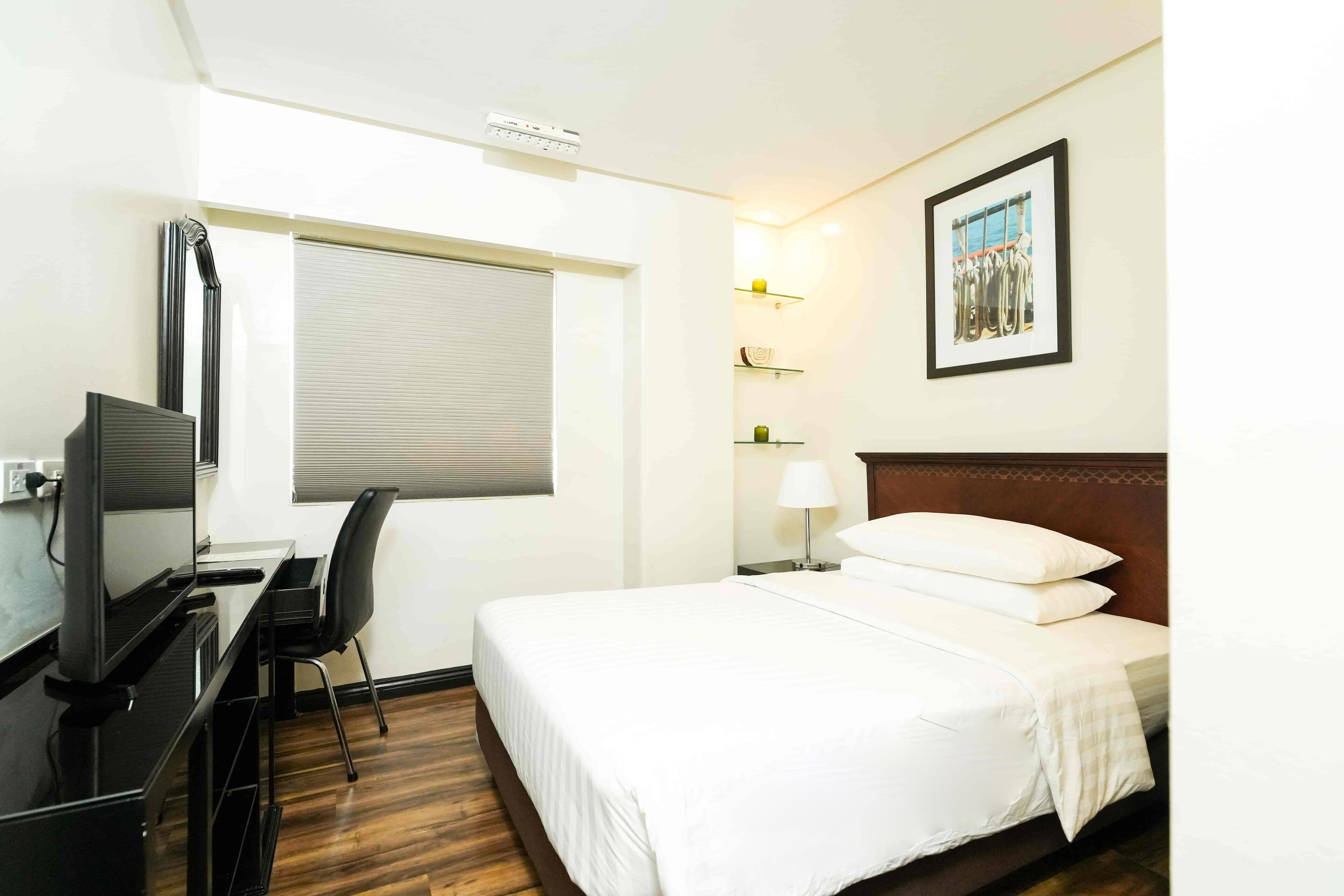A hotel room with a bed, desk, chair, and a window with blinds.