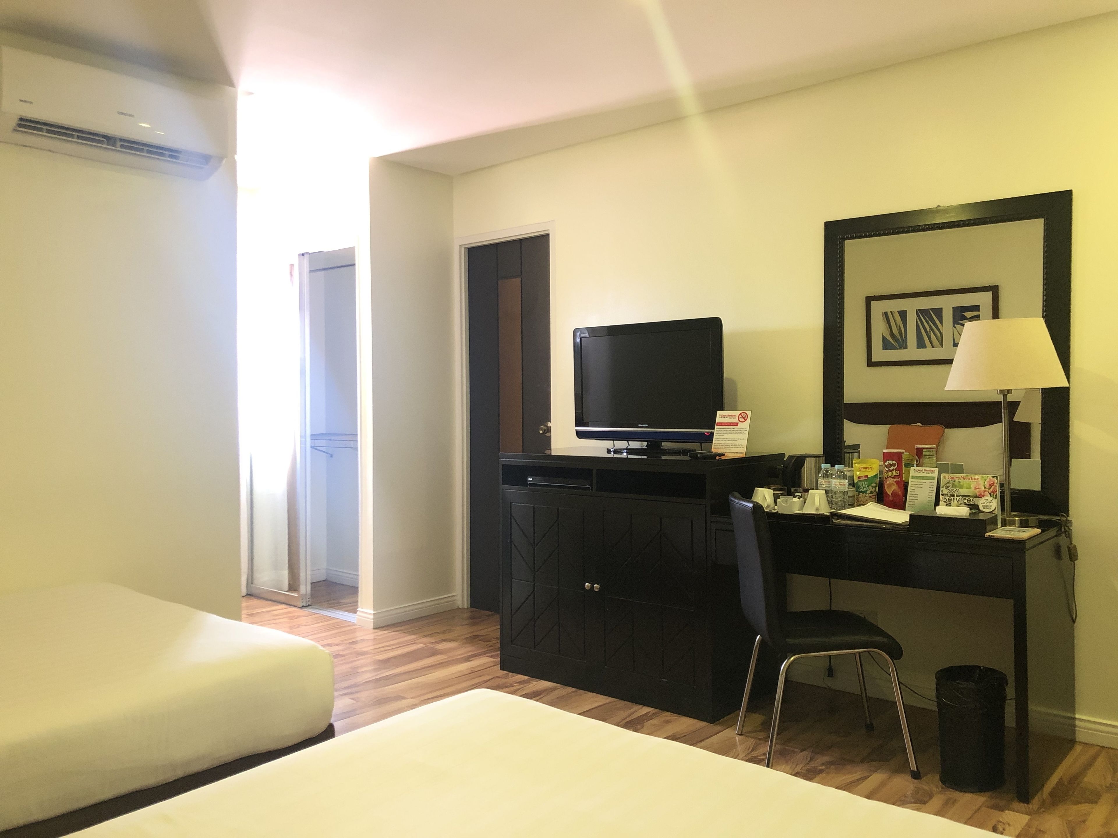 Een hotelkamer met een bed, een bureau met een computer, een stoel, een televisietoestel en een prullenbak.