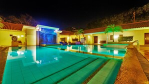 Piscina com cascata, espreguiçadeiras e uma pequena parede com cachoeira.