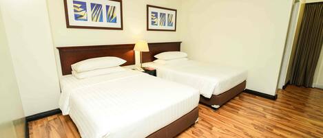 A hotel room with two beds, a wooden floor, and an air conditioning unit on the wall.