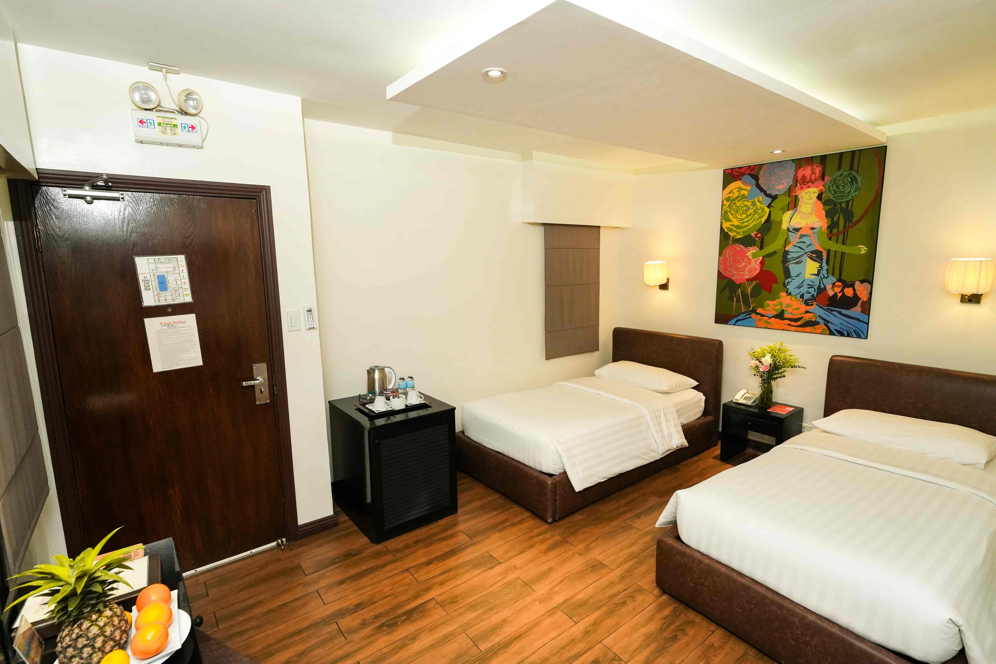 Habitación de hotel con dos camas, suelo de madera, un cuadro en la pared y una puerta con un cartel.