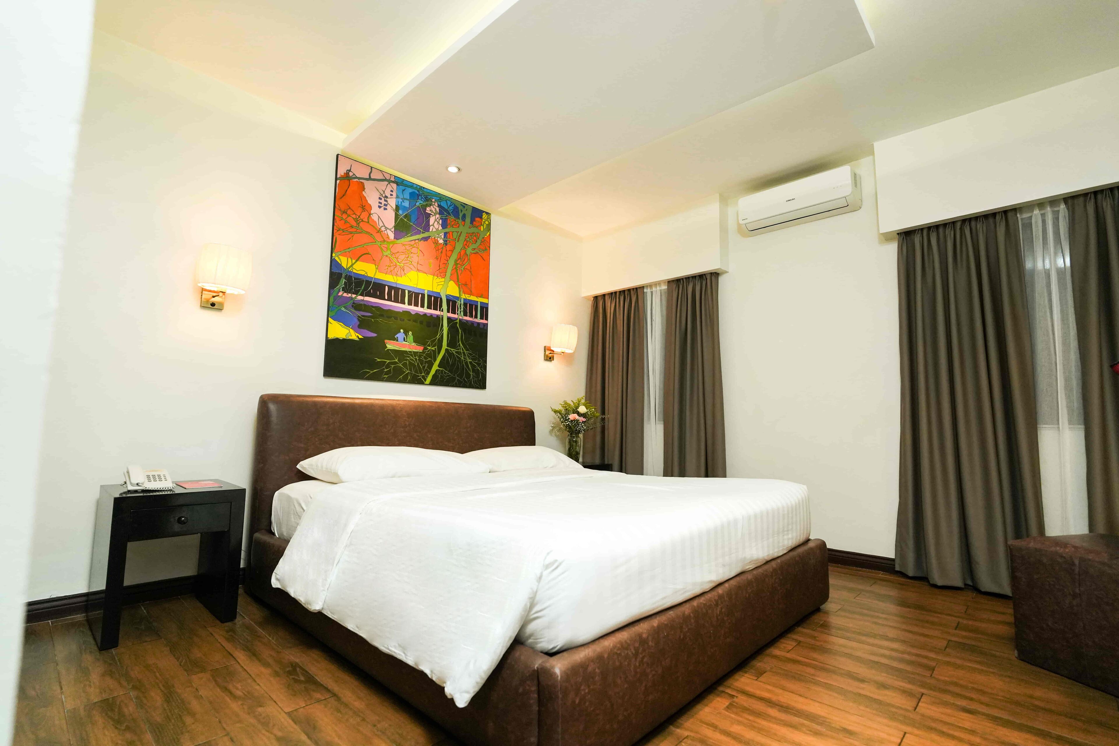 Habitación de hotel con una cama grande, una mesita de noche con teléfono, un cuadro en la pared y un equipo de aire acondicionado.