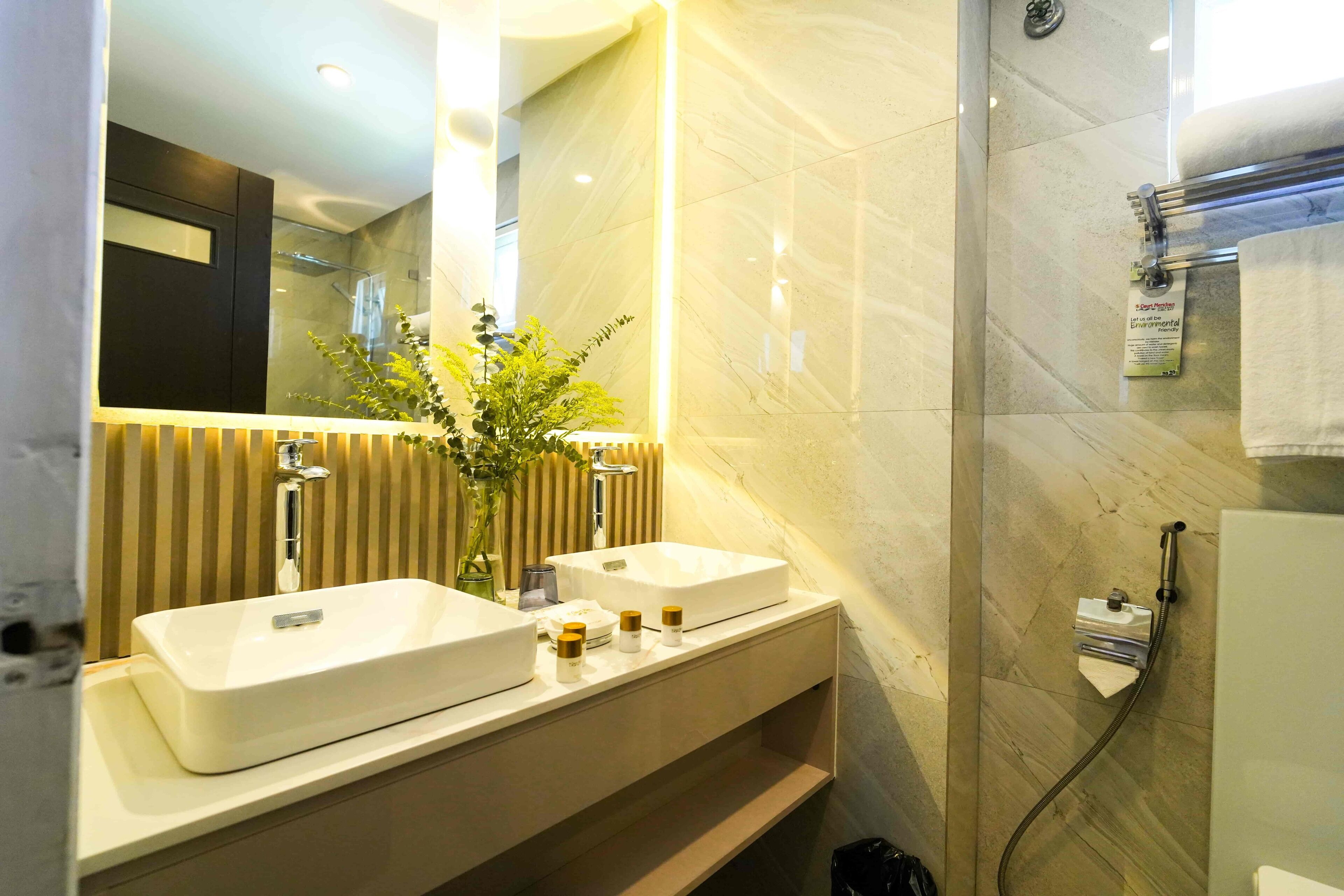 Un baño moderno con dos lavamanos, un espejo, una planta y una zona de ducha.