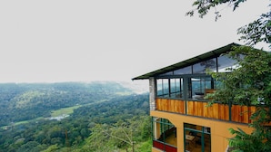 A modern two-story building with large windows and a wooden exterior, overlooking a lush valley. - Spice Tree Munnar (Udumbanchola)