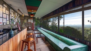 A restaurant with a long bench and tables, framed pictures on the wall, and a view of the landscape. - Spice Tree Munnar (Udumbanchola)