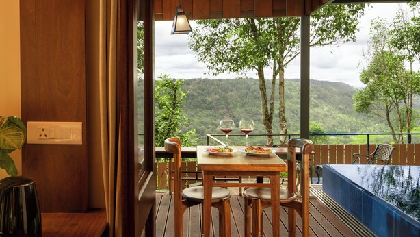 A wooden deck with a table and chairs, a hot tub, and a view of a forested hillside. - Spice Tree Munnar (Udumbanchola)