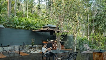 Un patio al aire libre con terraza de madera, sillas de metal y una mesa.