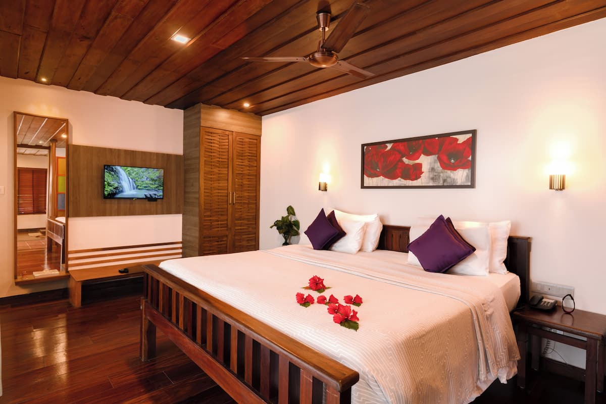 A neatly arranged hotel room with a large bed, wooden headboard, a television mounted on the wall, and a framed artwork above the bed.