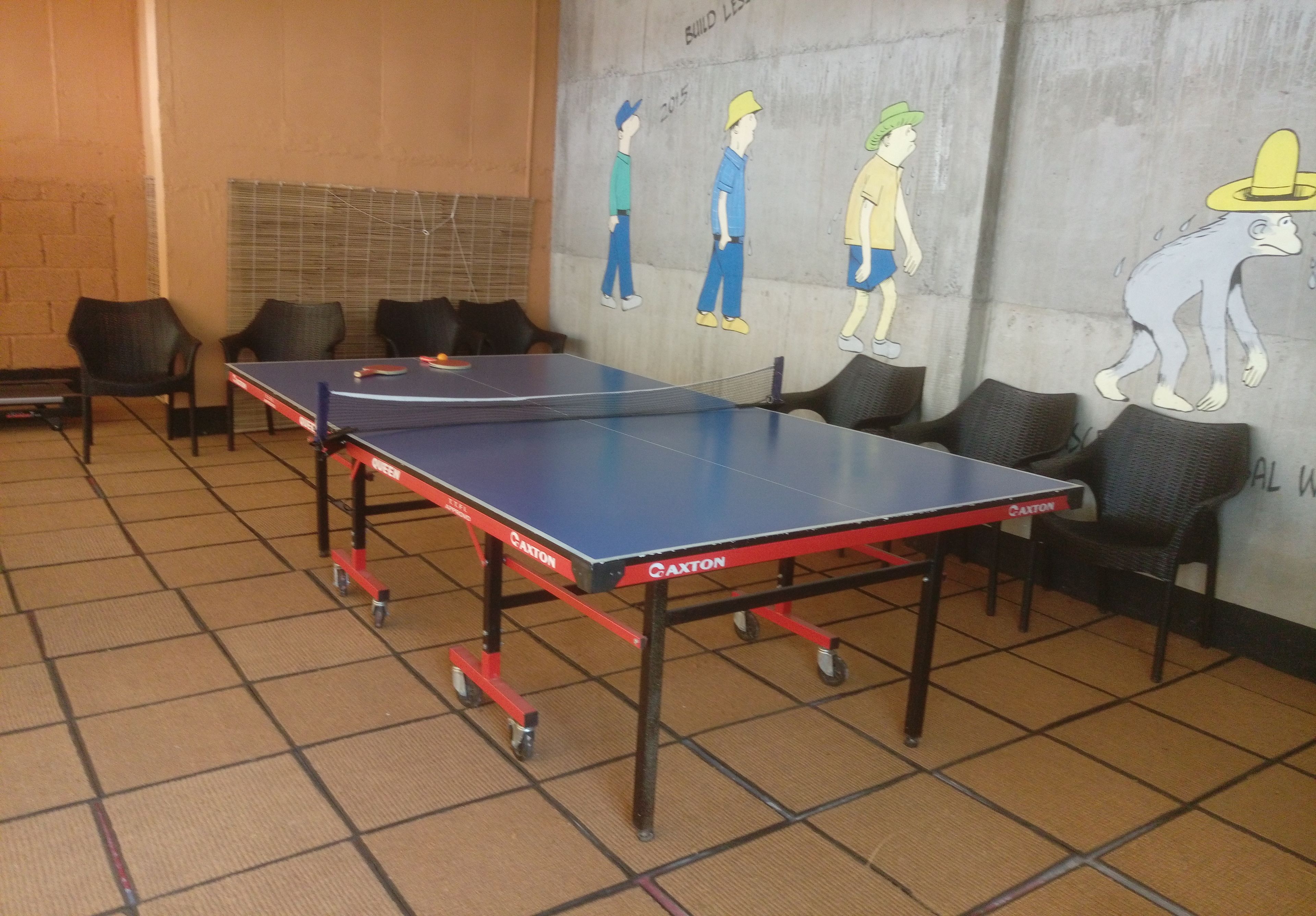 Een tafeltennistafel in een ruimte met stoelen en een muurschildering.