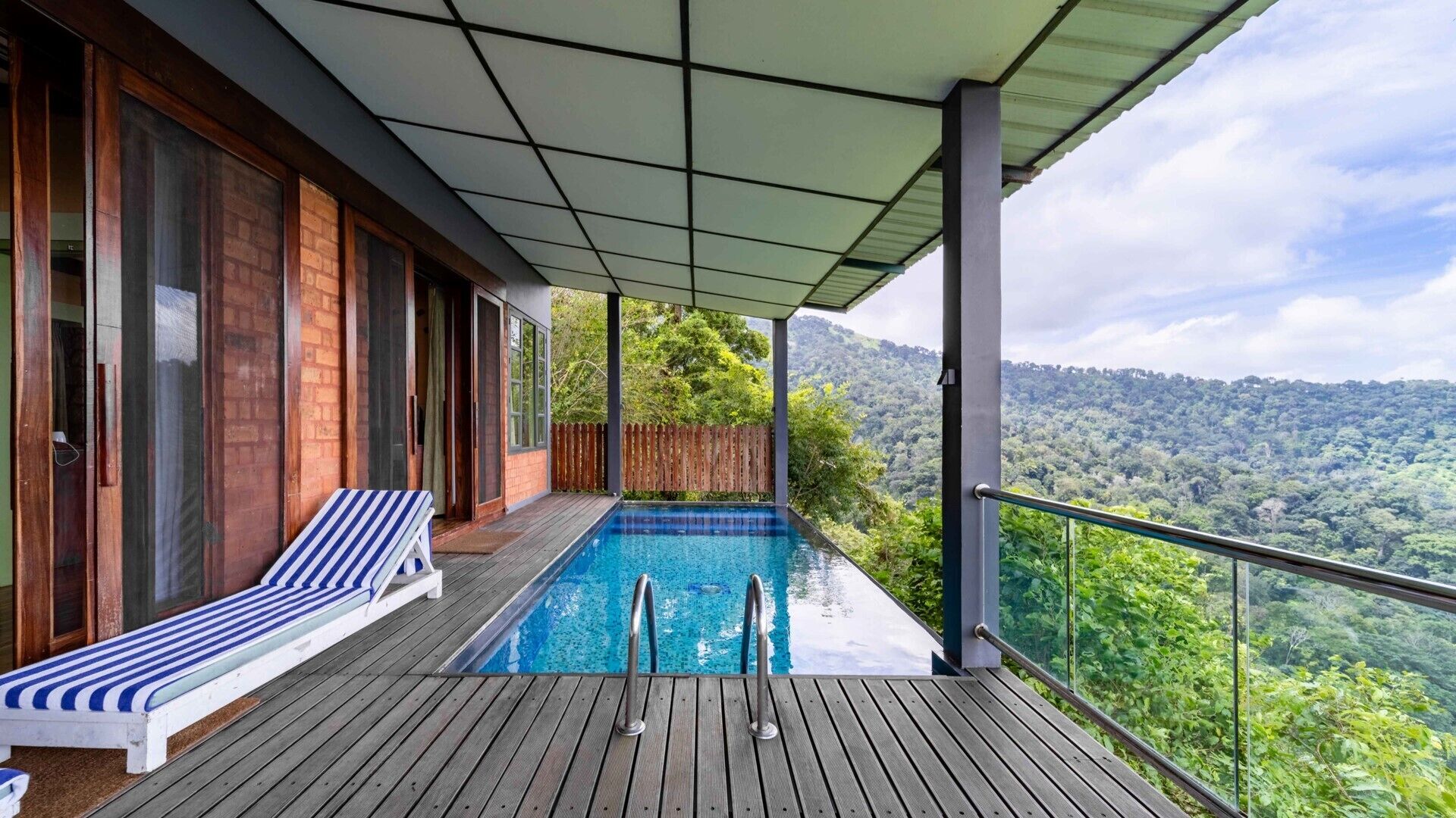 Um deck de madeira com piscina, uma espreguiçadeira e vista para uma cadeia montanhosa arborizada.