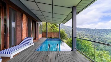 Um deck de madeira com piscina, uma espreguiçadeira e vista para uma cadeia montanhosa arborizada.