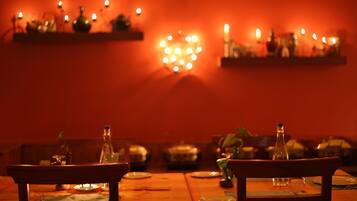 A dimly lit restaurant with tables set for dining, a heart-shaped light fixture on the wall, and candles on shelves.