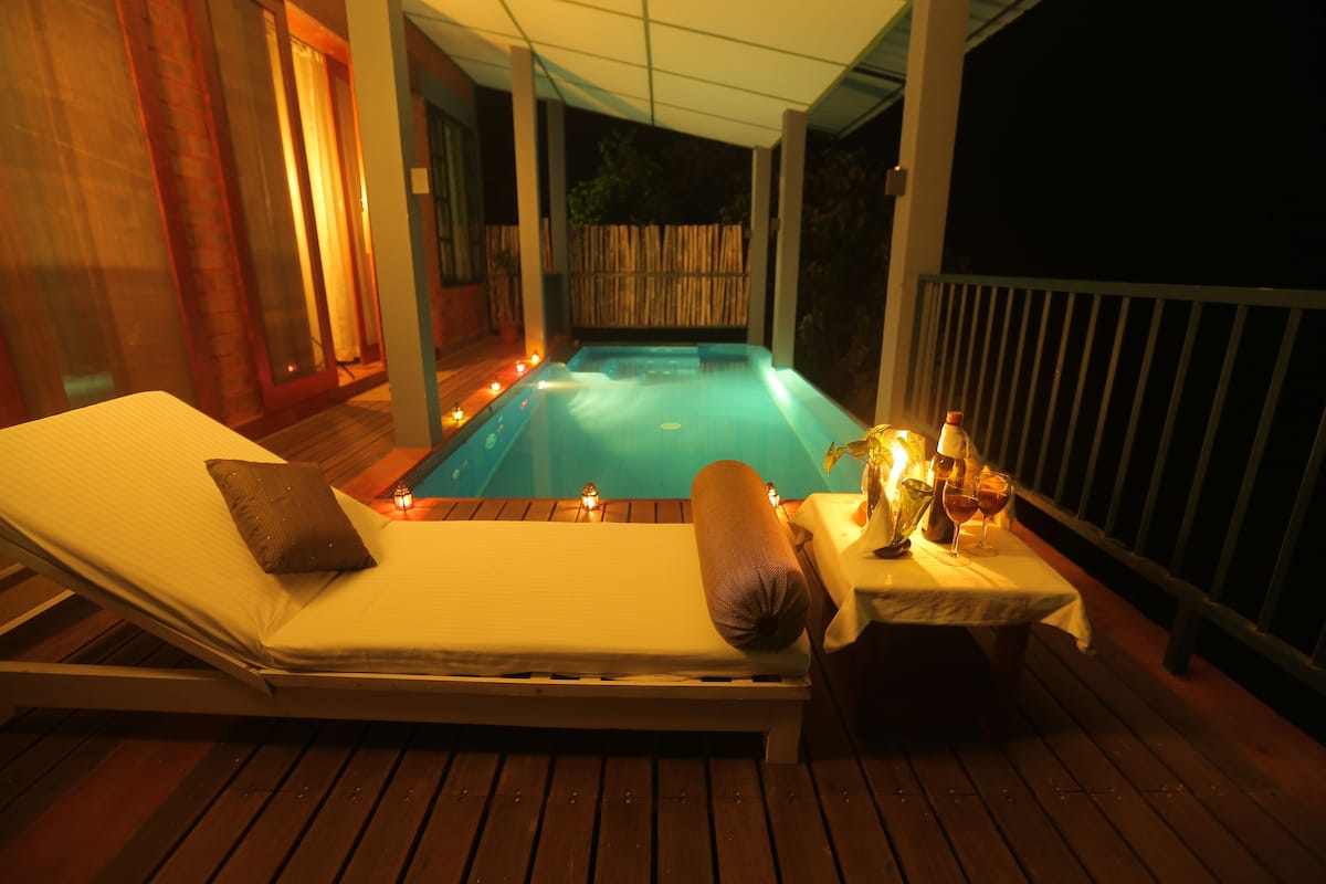 A poolside lounge with a reclining chair, a table with drinks, and candles.