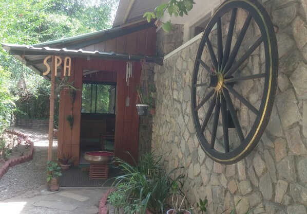 A spa entrance with a wooden facade, a stone wall, and a large black wheel.