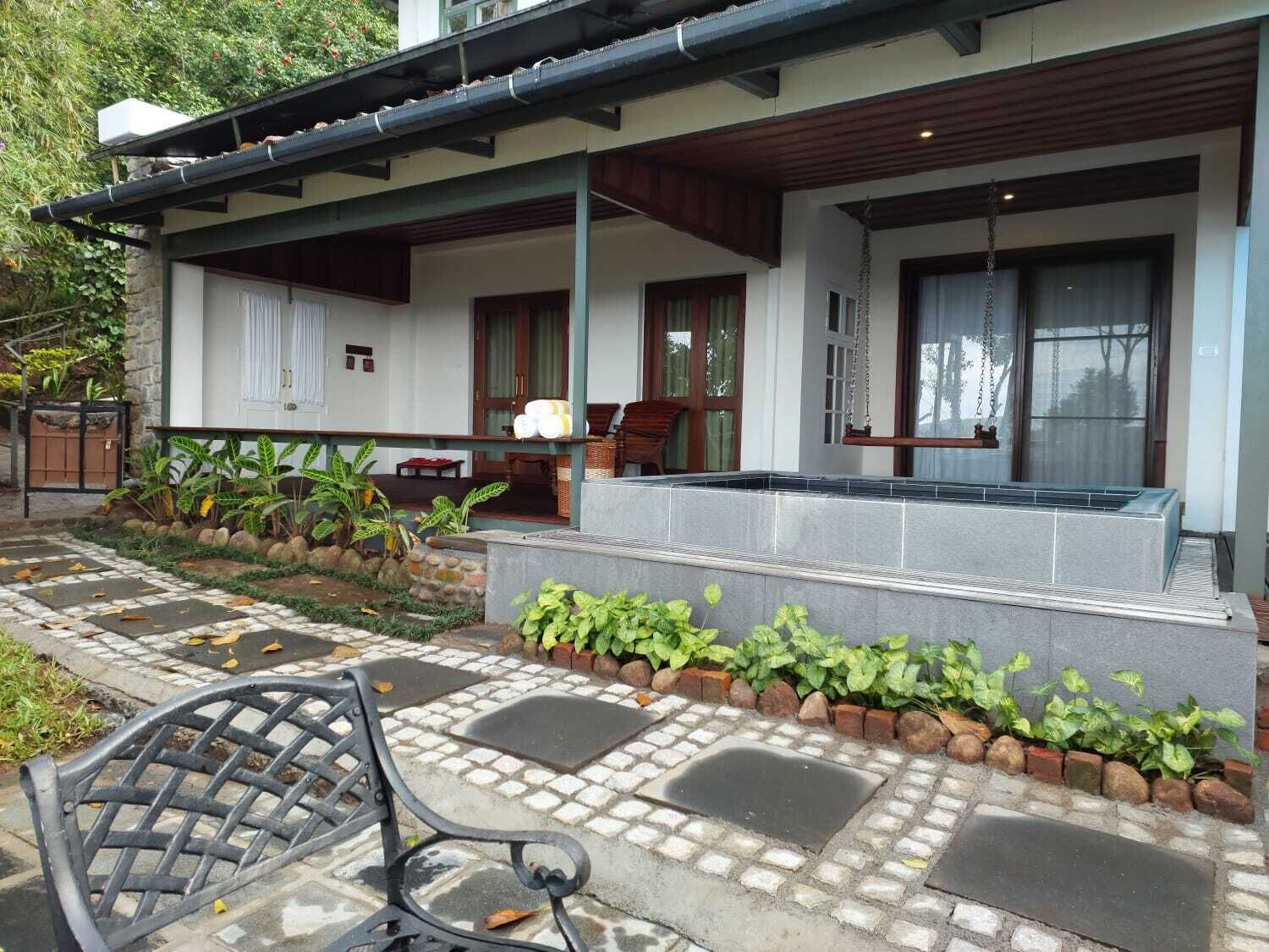 A covered outdoor seating area with a bench, a stone pathway, and a small garden with plants and a brick border.