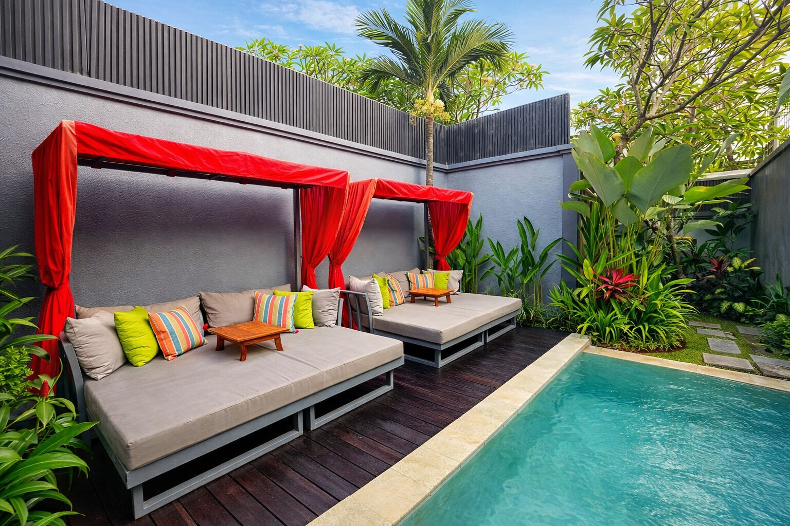 A poolside seating area with two sofas, red canopies, and a pool.