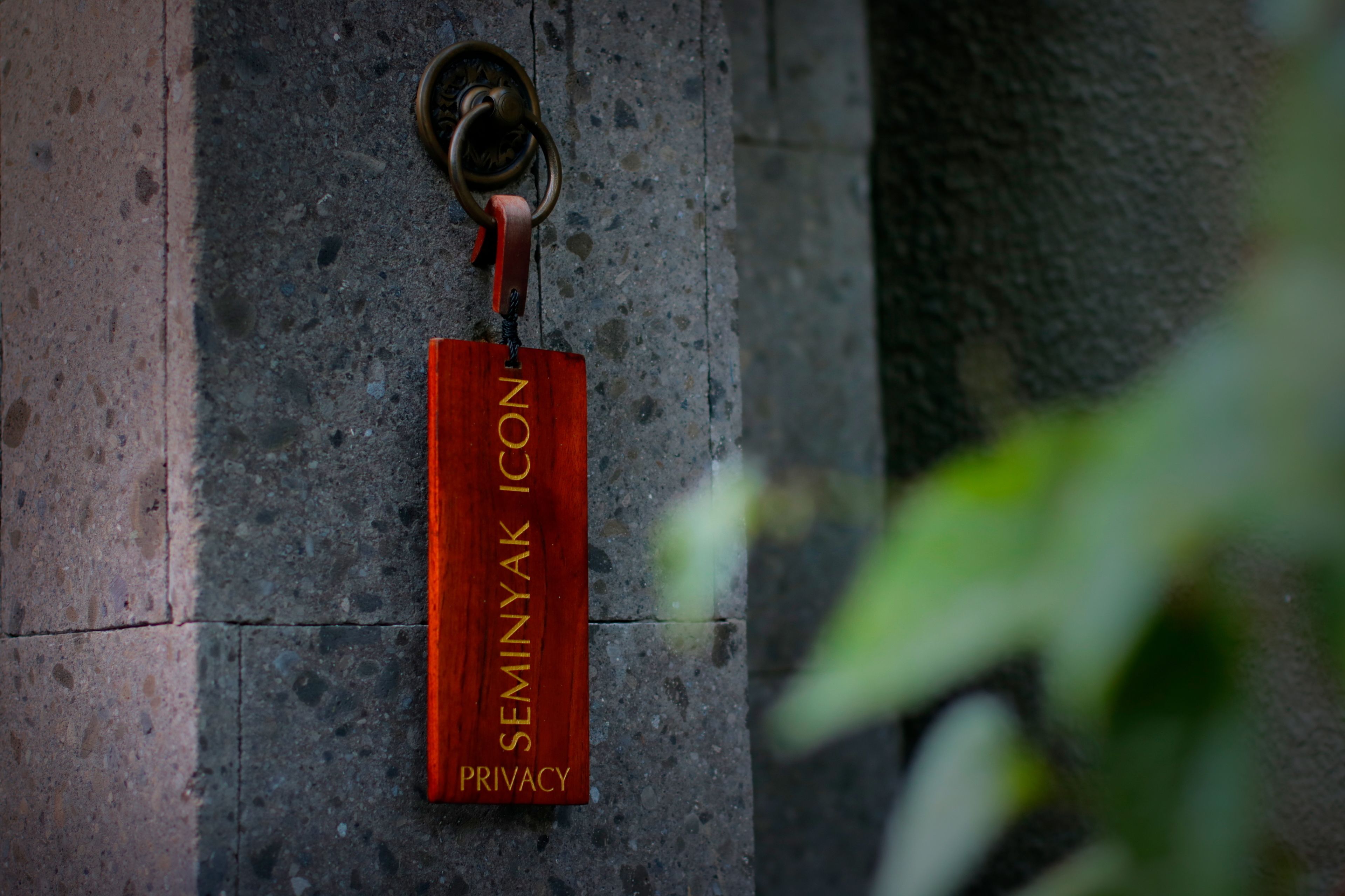 A red sign with the text "SEMINYAK ICON PRIVACY" mounted on a stone wall.
