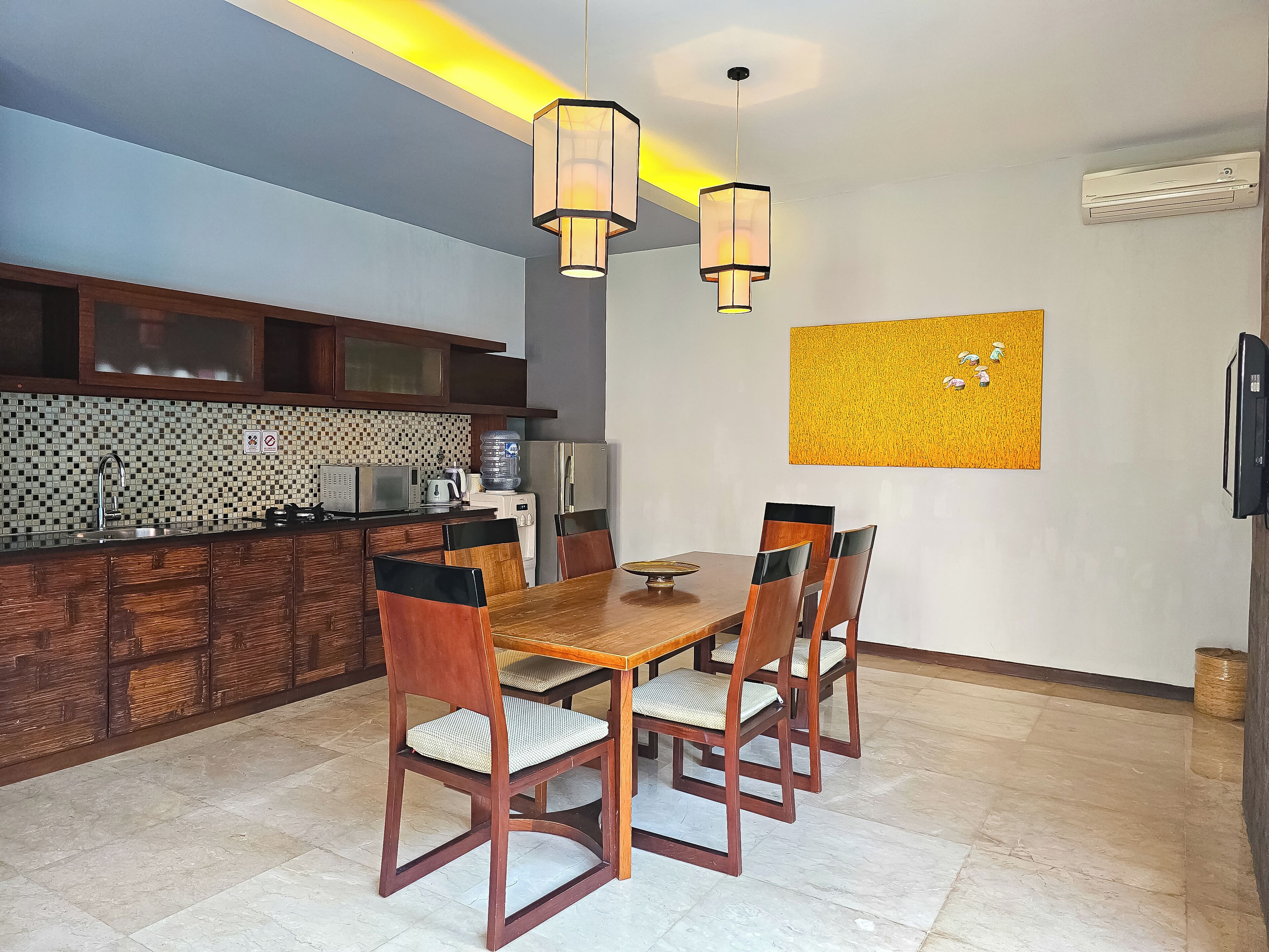 Uma sala de jantar com mesa e cadeiras de madeira, uma cozinha com revestimento de azulejos e iluminação pendente.