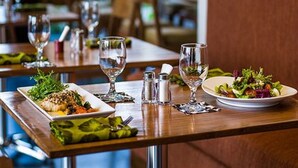 Ambiente de restaurante com mesas preparadas para refeições, incluindo pratos de comida e copos de vinho.