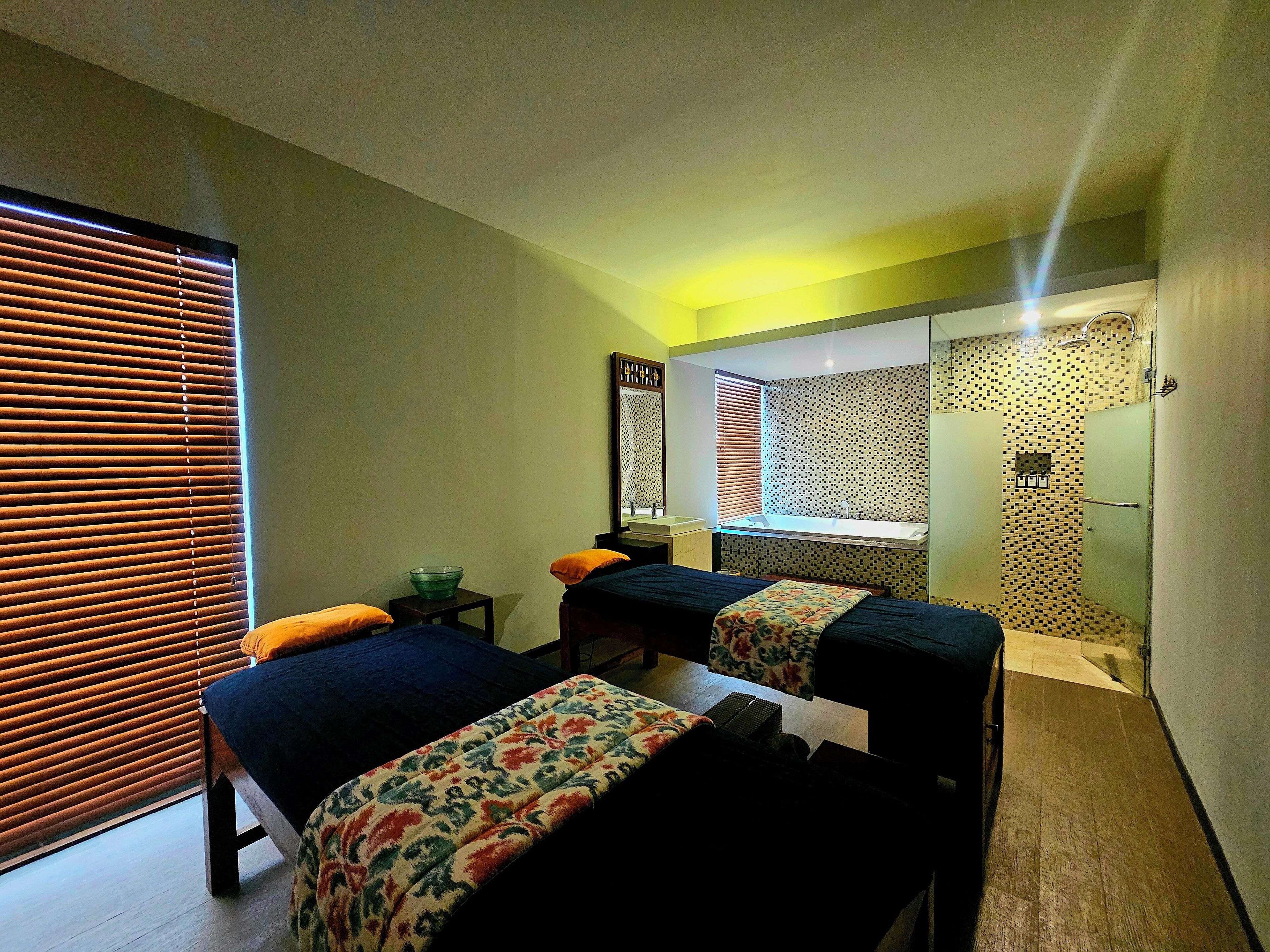 A hotel room with two beds, a bathroom with a shower, and a window with blinds.