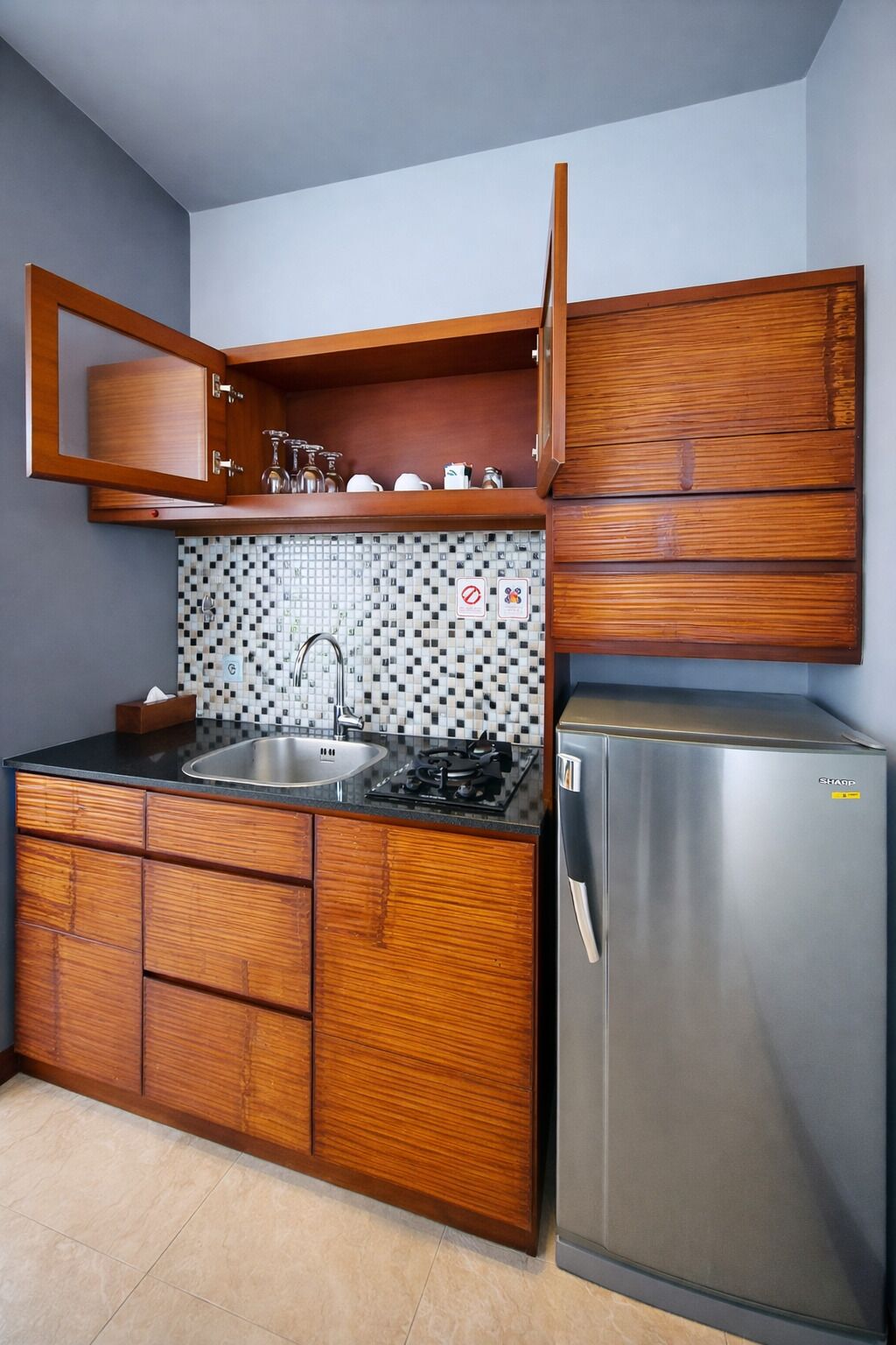 A compact kitchen with wooden cabinets, a stainless steel refrigerator, a tiled backsplash, and a gas stove.