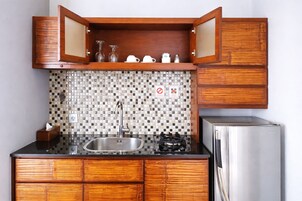 A compact kitchen with wooden cabinets, a tiled backsplash, a stainless steel sink, a gas stove, and a refrigerator.