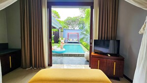 Quarto com cama, TV em aparador de madeira, e vista para piscina e área de estar ao ar livre.
