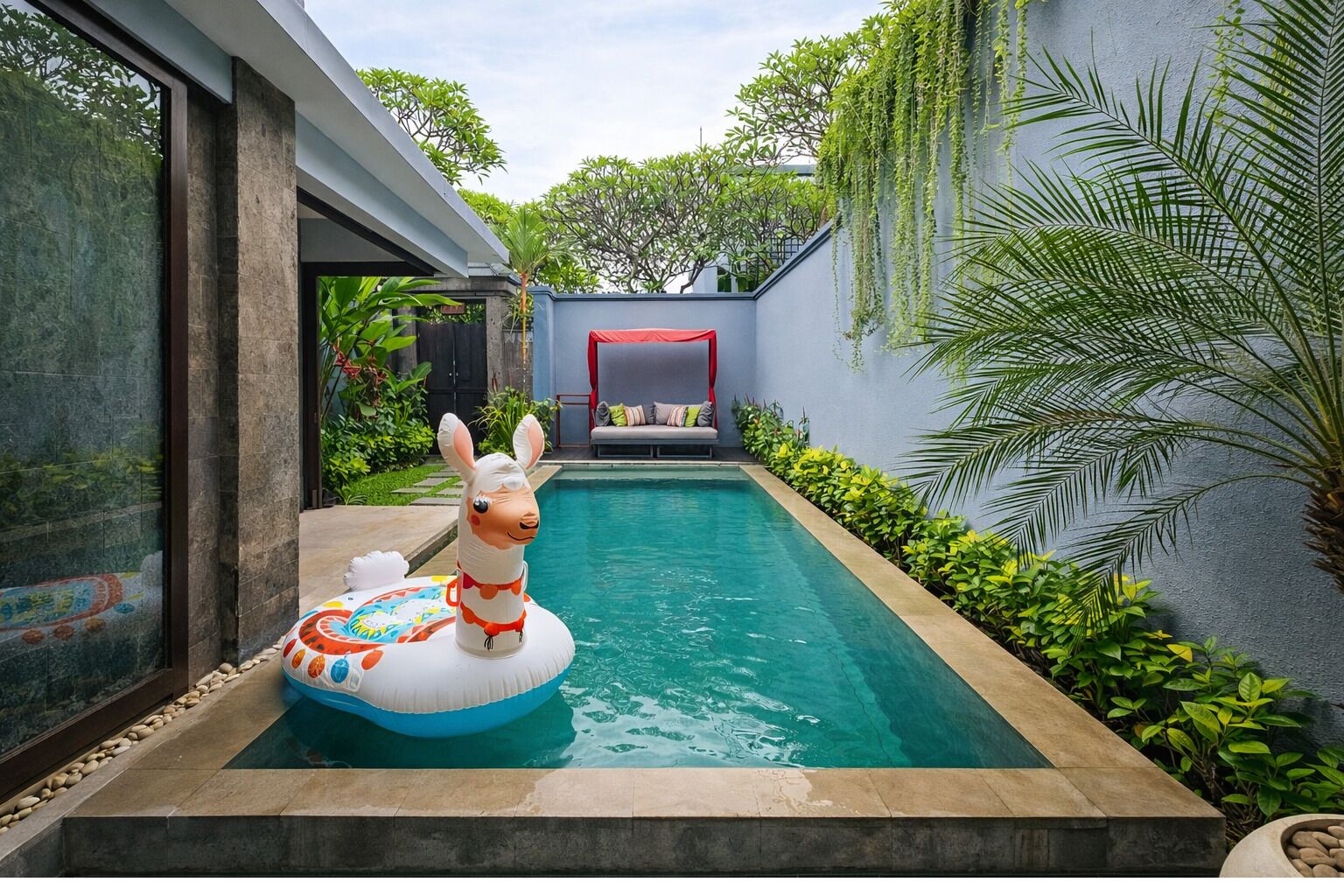A swimming pool with a llama float, surrounded by greenery and a modern building.