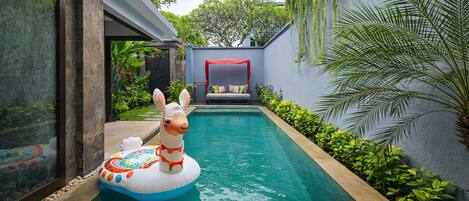 A swimming pool with a llama float, surrounded by greenery and a modern building.