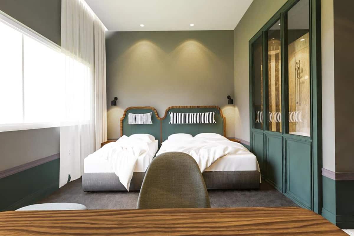 Une chambre d’hôtel avec deux lits, un bureau en bois et une grande fenêtre avec des rideaux.