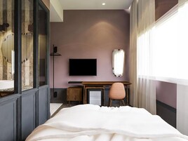 Una habitación de hotel moderna con una cama grande, un escritorio, una silla, un televisor y un ventanal con cortinas.