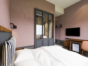 A hotel room with a bed, a wardrobe, a television, and a desk with a chair.