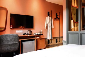 Een hotelkamer met een bed, een bureau met een computer, een televisie, een minibar, een badjas en een spiegel.