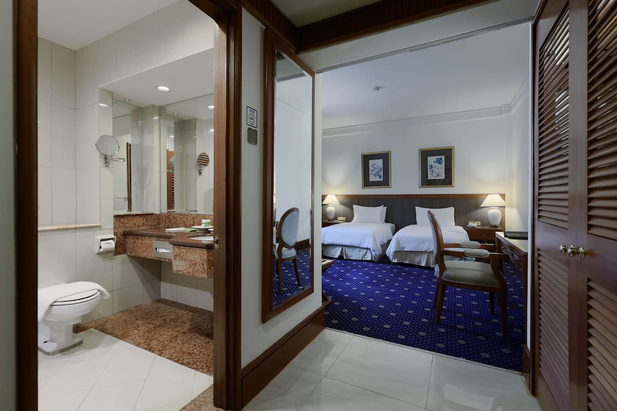 Une chambre d’hôtel avec une salle de bain, un lit avec deux oreillers, une table de chevet, une chaise et un miroir.