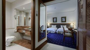 A hotel room with a bathroom, a bed with two pillows, a nightstand, a chair, and a mirror.