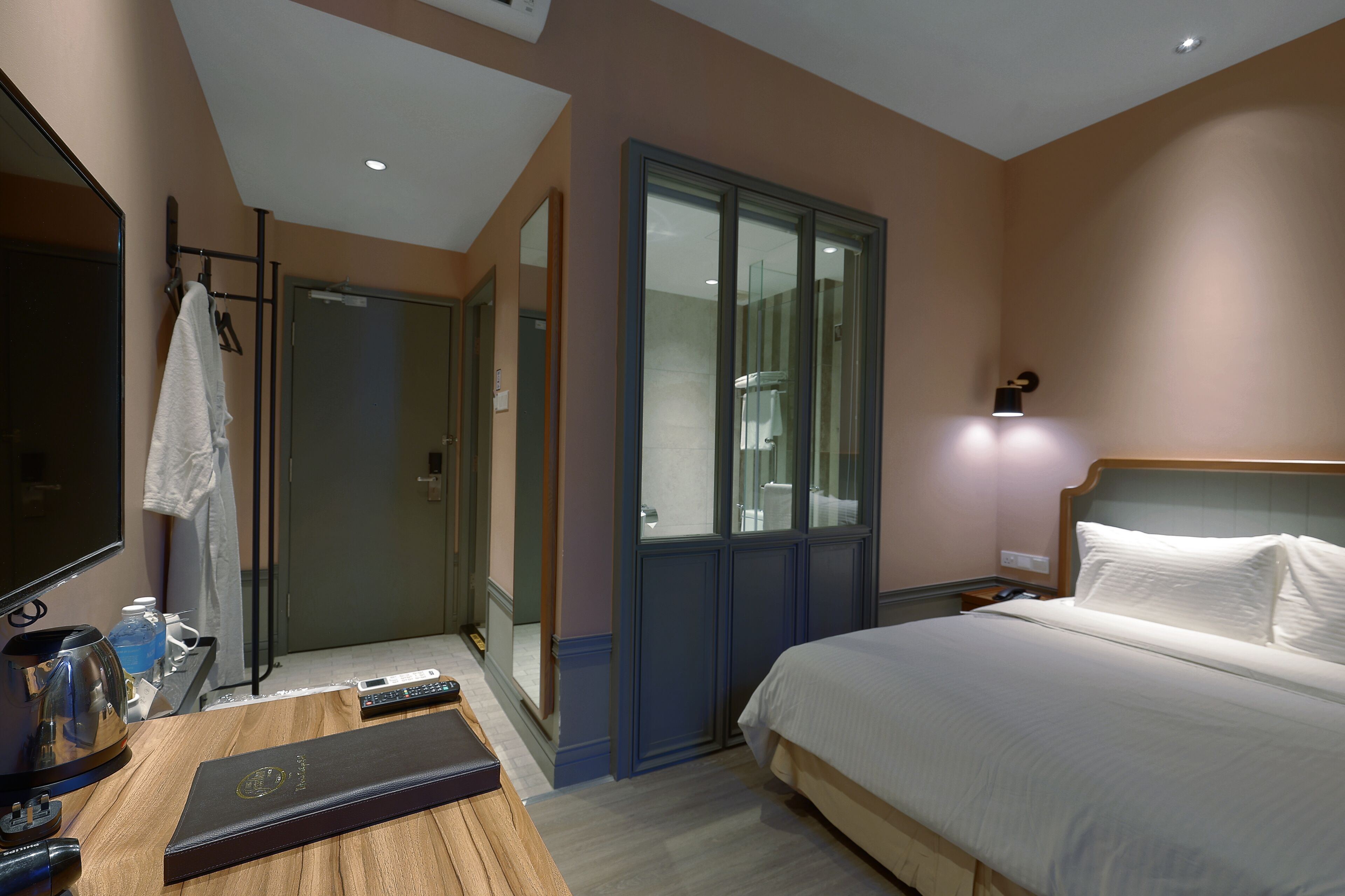 A hotel room with a bed, a desk with a laptop, a mirror, and a wardrobe.