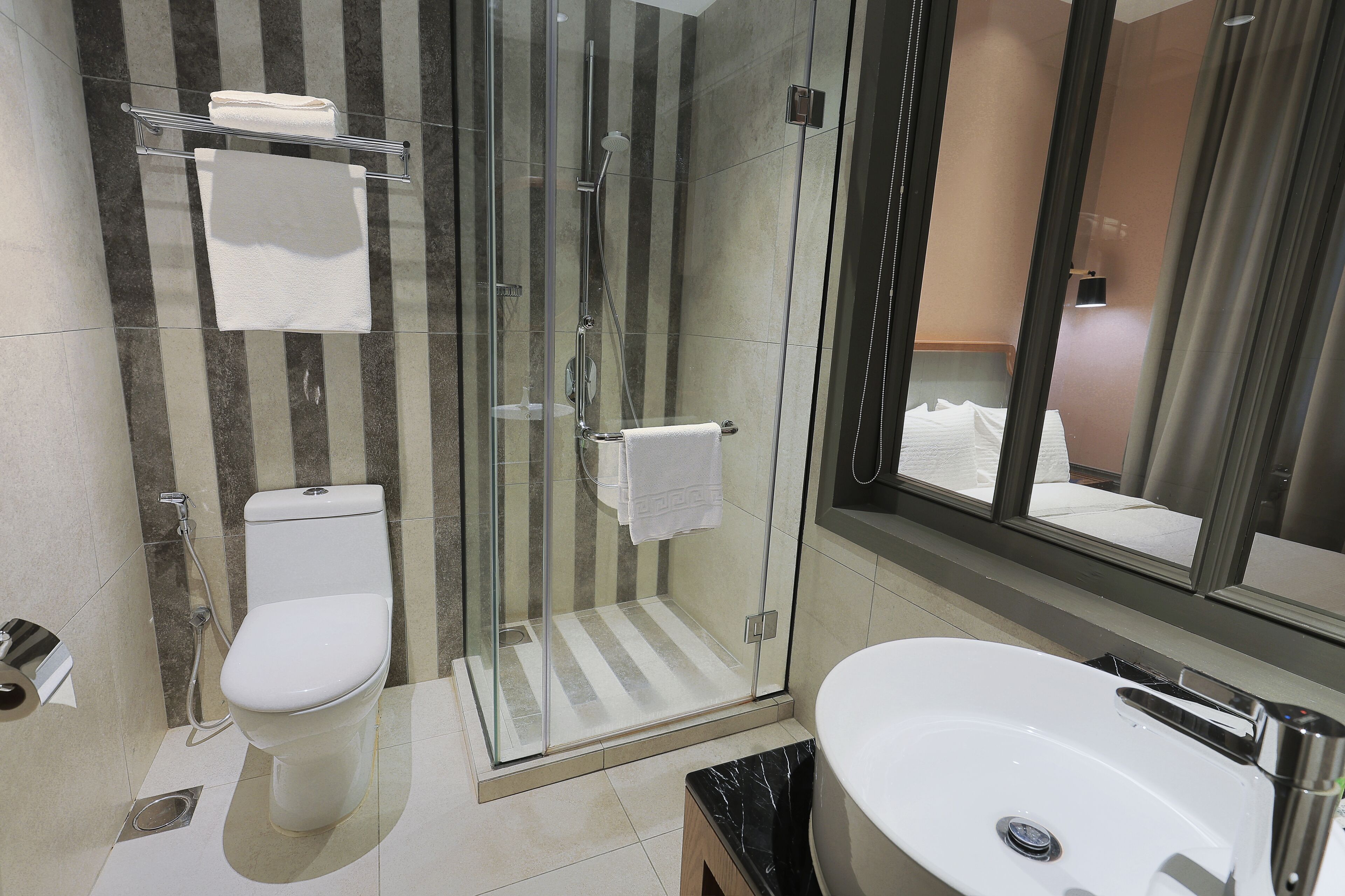 A modern bathroom with a glass-enclosed shower, a toilet, and a sink with a marble countertop.