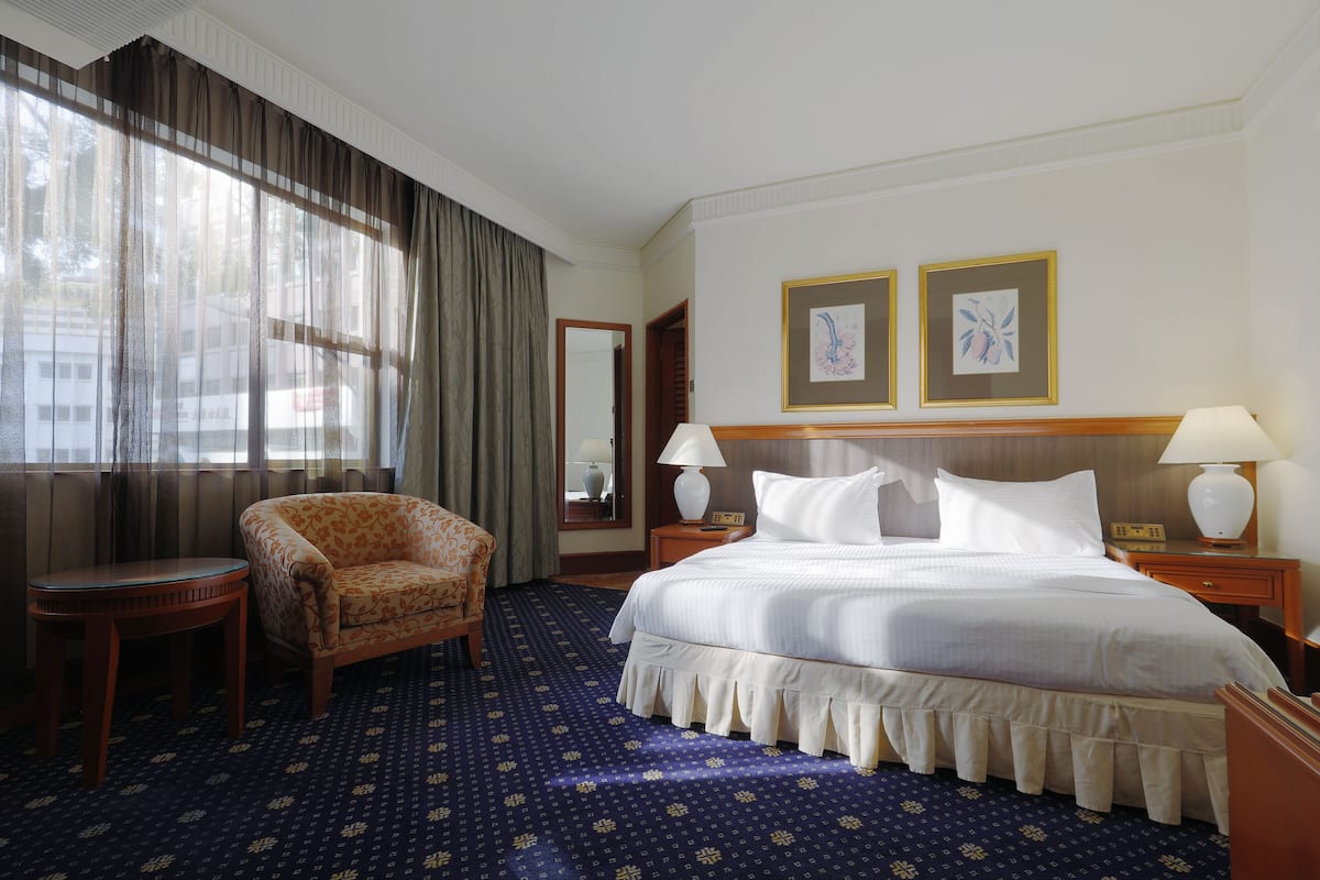 Une chambre d’hôtel avec un grand lit, une chaise, deux tables de chevet avec des lampes, un miroir et deux tableaux encadrés au mur.
