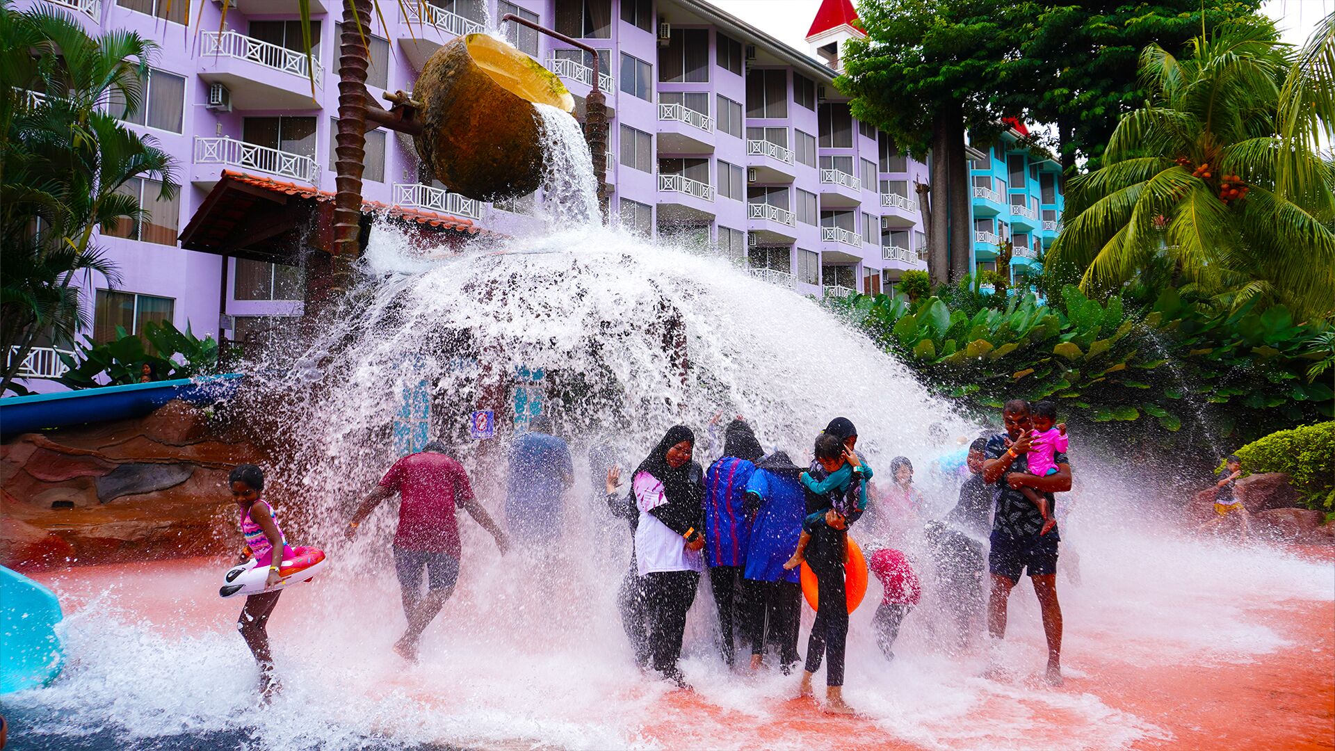 A water play area with a large water fountain and a building with balconies in the background.