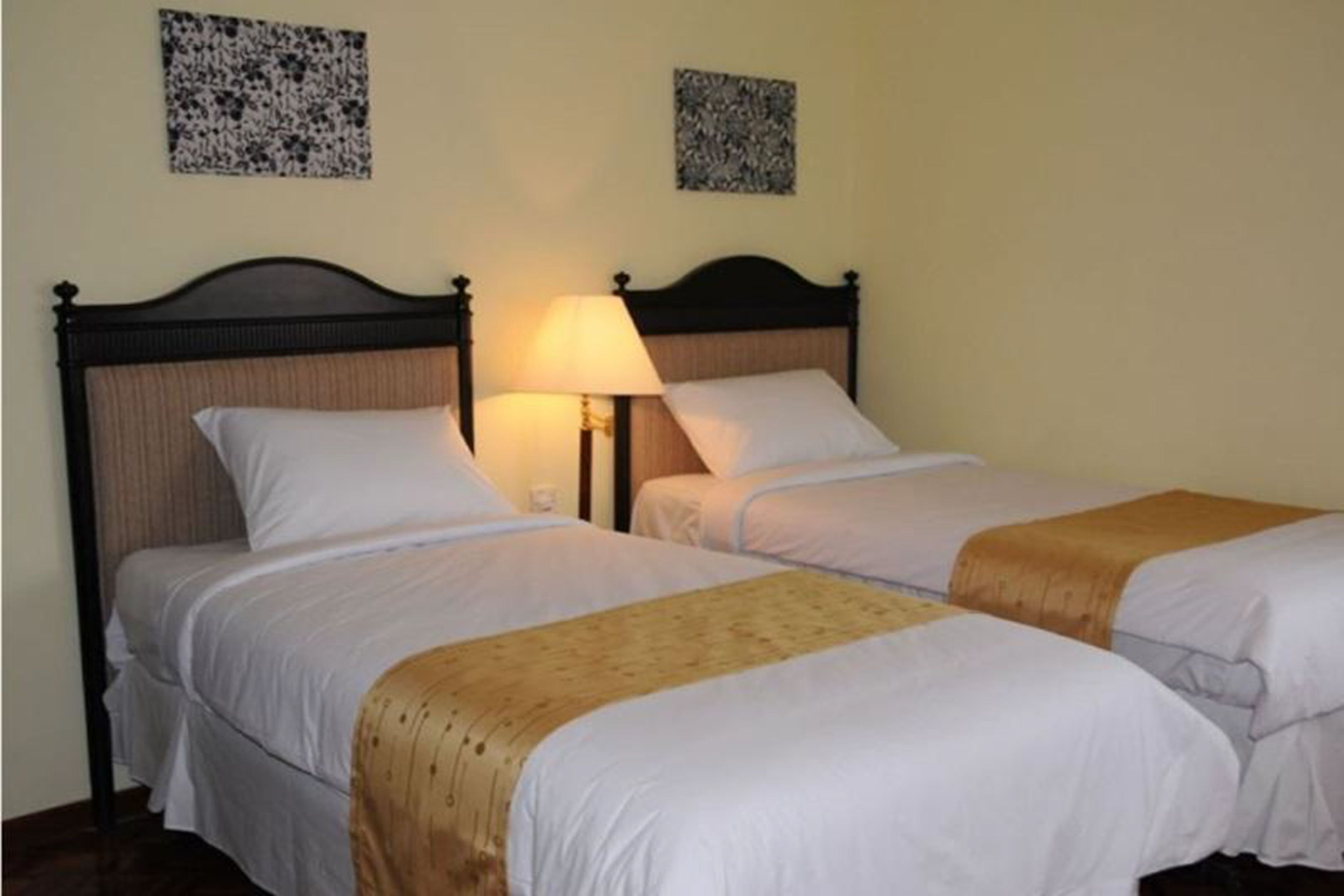 Une chambre d’hôtel avec deux lits simples, une tête de lit en bois, une lampe de chevet et deux tableaux encadrés au mur.