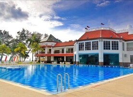 Piscina com superfície de água azul cristalina, rodeada por um edifício com telhado vermelho e paredes brancas.