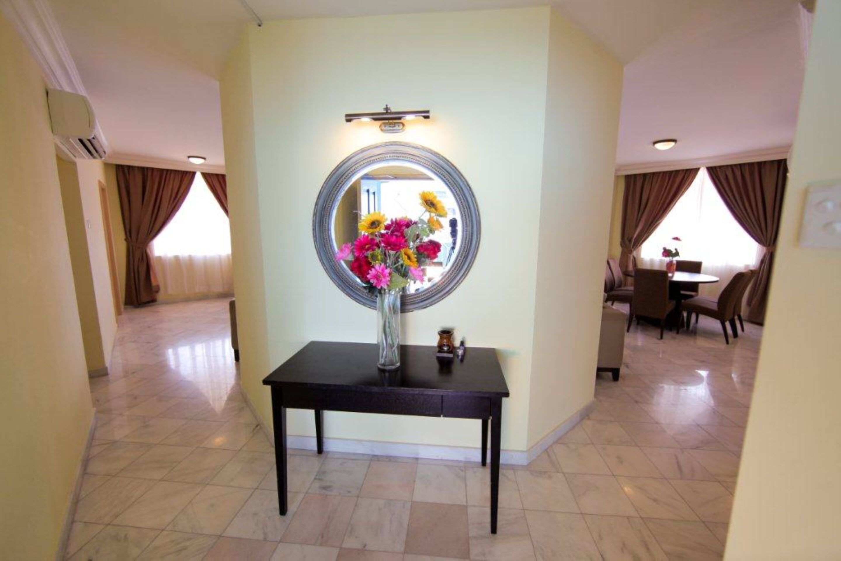 Un hall d’hôtel avec un grand miroir rond, un vase rempli de fleurs, une petite table et, au fond, un espace repas.