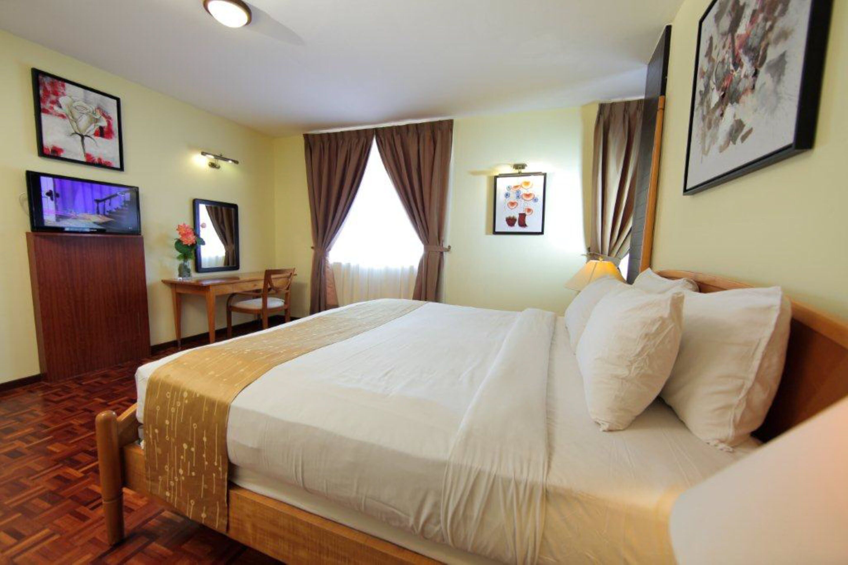 A hotel room with a large bed, a desk with a chair, a television, and artwork on the walls.